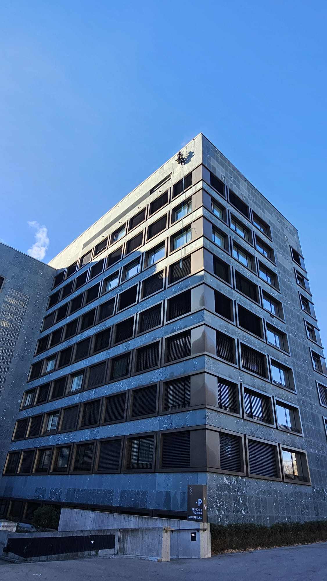 Høj bygning med industriklatrer ved tagkanten mod blå himmel