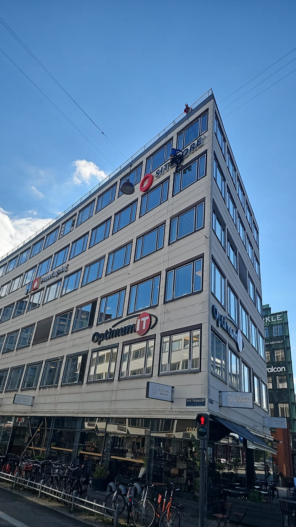 Tekniker i reb ved facadeskilt på høj bygning med Optimum IT-skilt