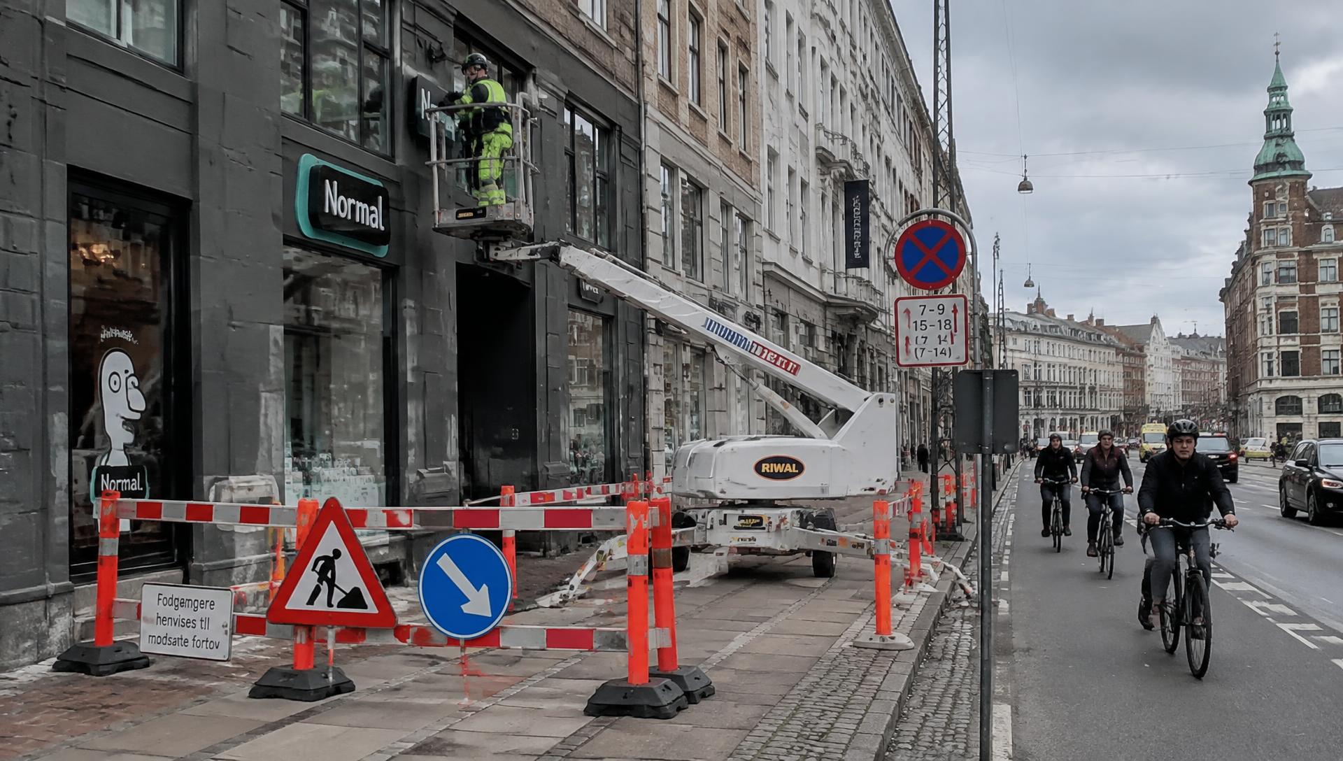 Afspærret arbejdsområde med lift, afspærringshegn, kegler og midlertidige trafikskilte i dansk bymiljø